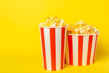 Patlamış mısır kutusu. Arka planda kırmızı ve beyaz çizgili patlamış mısır kovaları. Sinema ve eğlence anlayışı. Patlamış mısırla film gecesi. Peynirli patlamış mısır. Lezzetli aperatif, aperatif. Metin için yer.