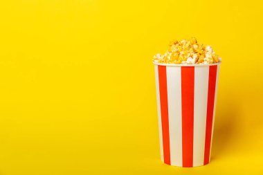 Patlamış mısır kutusu. Arka planda kırmızı ve beyaz çizgili patlamış mısır kovaları. Sinema ve eğlence anlayışı. Patlamış mısırla film gecesi. Peynirli patlamış mısır. Lezzetli aperatif, aperatif. Metin için yer.