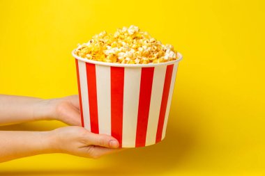 Patlamış mısır kutusu. Arka planda kırmızı ve beyaz çizgili patlamış mısır kovaları. Sinema ve eğlence anlayışı. Patlamış mısırla film gecesi. Peynirli patlamış mısır. Lezzetli aperatif, aperatif. Metin için yer.