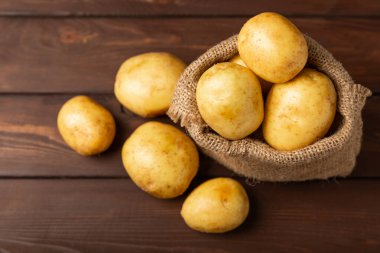 Genç patatesler Ahşap zeminde taze patates. Çuvalda patates. Hasat koleksiyonu. organik, taze kazılmış patatesler. Tarım geçmişi. Vejetaryen. Sebzeler. Mesajlar için yer. Boşluğu kopyala