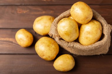 Genç patatesler Ahşap zeminde taze patates. Çuvalda patates. Hasat koleksiyonu. organik, taze kazılmış patatesler. Tarım geçmişi. Vejetaryen. Sebzeler. Mesajlar için yer. Boşluğu kopyala