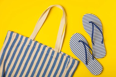 Plaj çantası, hasır şapka ve parlak renkli arka planda sandaletler. Plaj objesi. Yaz modasına uygun bir çanta. Plaj aksesuarları. Yaz tatili konsepti. Mesaj için uygun bir yer. Boşluğu kopyala. Üst görünüm