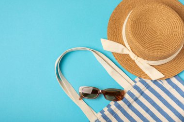 Plaj çantası, hasır şapka ve parlak renkli arka planda sandaletler. Plaj objesi. Yaz modasına uygun bir çanta. Plaj aksesuarları. Yaz tatili konsepti. Mesaj için uygun bir yer. Boşluğu kopyala. Üst görünüm