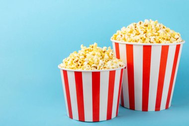 Patlamış mısır kutusu. Renkli arka planda kırmızı ve beyaz çizgili patlamış mısır kovaları. Sinema ve eğlence anlayışı. Patlamış mısırla film gecesi. Lezzetli aperatif, aperatif. Metin için yer.