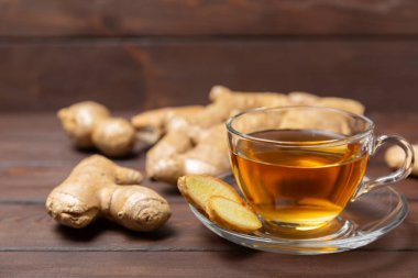 Tahta zemin üzerinde zencefil kökü dilimleri olan bir fincan sıcak zencefil çayı. Isıtıcı içecek. Alternatif tıp. Ballı, limonlu, zencefilli ve naneli çay. Mesaj için yer var. Boşluğu kopyala