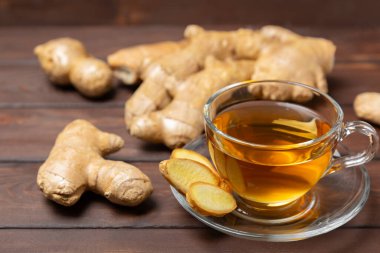 Tahta zemin üzerinde zencefil kökü dilimleri olan bir fincan sıcak zencefil çayı. Isıtıcı içecek. Alternatif tıp. Ballı, limonlu, zencefilli ve naneli çay. Mesaj için yer var. Boşluğu kopyala