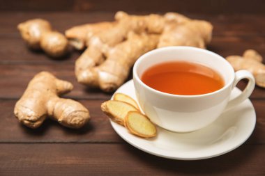 Tahta zemin üzerinde zencefil kökü dilimleri olan bir fincan sıcak zencefil çayı. Isıtıcı içecek. Alternatif tıp. Ballı, limonlu, zencefilli ve naneli çay. Mesaj için yer var. Boşluğu kopyala