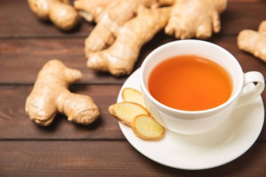 Tahta zemin üzerinde zencefil kökü dilimleri olan bir fincan sıcak zencefil çayı. Isıtıcı içecek. Alternatif tıp. Ballı, limonlu, zencefilli ve naneli çay. Mesaj için yer var. Boşluğu kopyala