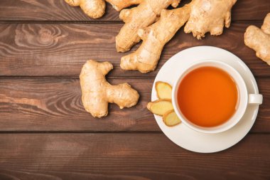 Tahta zemin üzerinde zencefil kökü dilimleri olan bir fincan sıcak zencefil çayı. Isıtıcı içecek. Alternatif tıp. Ballı, limonlu, zencefilli ve naneli çay. Mesaj için yer var. Boşluğu kopyala