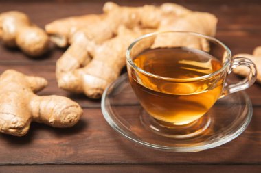 Tahta zemin üzerinde zencefil kökü dilimleri olan bir fincan sıcak zencefil çayı. Isıtıcı içecek. Alternatif tıp. Ballı, limonlu, zencefilli ve naneli çay. Mesaj için yer var. Boşluğu kopyala