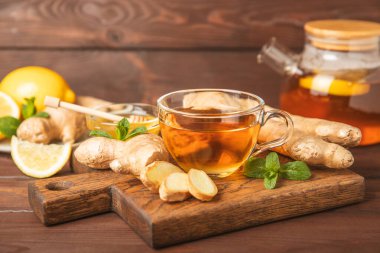 Tahta zemin üzerinde zencefil kökü dilimleri olan bir fincan sıcak zencefil çayı. Isıtıcı içecek. Alternatif tıp. Ballı, limonlu, zencefilli ve naneli çay. Mesaj için yer var. Boşluğu kopyala