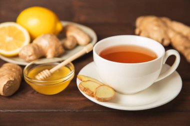 Tahta zemin üzerinde zencefil kökü dilimleri olan bir fincan sıcak zencefil çayı. Isıtıcı içecek. Alternatif tıp. Ballı, limonlu, zencefilli ve naneli çay. Mesaj için yer var. Boşluğu kopyala