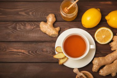 Tahta zemin üzerinde zencefil kökü dilimleri olan bir fincan sıcak zencefil çayı. Isıtıcı içecek. Alternatif tıp. Ballı, limonlu, zencefilli ve naneli çay. Mesaj için yer var. Boşluğu kopyala