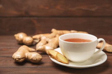 Tahta zemin üzerinde zencefil kökü dilimleri olan bir fincan sıcak zencefil çayı. Isıtıcı içecek. Alternatif tıp. Ballı, limonlu, zencefilli ve naneli çay. Mesaj için yer var. Boşluğu kopyala
