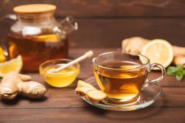 Tahta zemin üzerinde zencefil kökü dilimleri olan bir fincan sıcak zencefil çayı. Isıtıcı içecek. Alternatif tıp. Ballı, limonlu, zencefilli ve naneli çay. Mesaj için yer var. Boşluğu kopyala