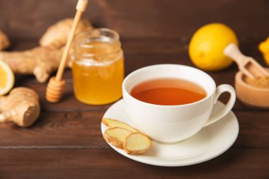 Tahta zemin üzerinde zencefil kökü dilimleri olan bir fincan sıcak zencefil çayı. Isıtıcı içecek. Alternatif tıp. Ballı, limonlu, zencefilli ve naneli çay. Mesaj için yer var. Boşluğu kopyala