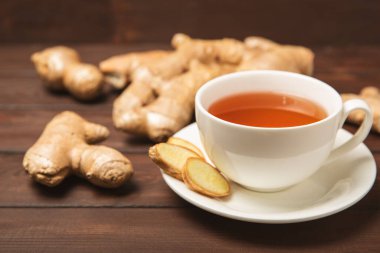 Tahta zemin üzerinde zencefil kökü dilimleri olan bir fincan sıcak zencefil çayı. Isıtıcı içecek. Alternatif tıp. Ballı, limonlu, zencefilli ve naneli çay. Mesaj için yer var. Boşluğu kopyala