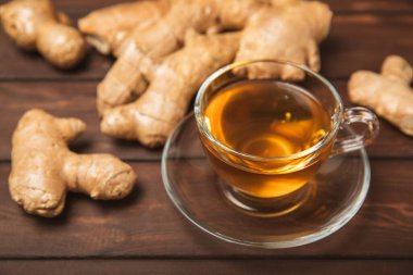 Tahta zemin üzerinde zencefil kökü dilimleri olan bir fincan sıcak zencefil çayı. Isıtıcı içecek. Alternatif tıp. Ballı, limonlu, zencefilli ve naneli çay. Mesaj için yer var. Boşluğu kopyala
