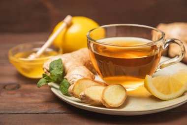 Tahta zemin üzerinde zencefil kökü dilimleri olan bir fincan sıcak zencefil çayı. Isıtıcı içecek. Alternatif tıp. Ballı, limonlu, zencefilli ve naneli çay. Mesaj için yer var. Boşluğu kopyala