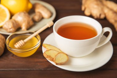 Tahta zemin üzerinde zencefil kökü dilimleri olan bir fincan sıcak zencefil çayı. Isıtıcı içecek. Alternatif tıp. Ballı, limonlu, zencefilli ve naneli çay. Mesaj için yer var. Boşluğu kopyala