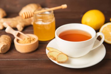 Tahta zemin üzerinde zencefil kökü dilimleri olan bir fincan sıcak zencefil çayı. Isıtıcı içecek. Alternatif tıp. Ballı, limonlu, zencefilli ve naneli çay. Mesaj için yer var. Boşluğu kopyala