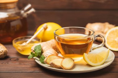 Tahta zemin üzerinde zencefil kökü dilimleri olan bir fincan sıcak zencefil çayı. Isıtıcı içecek. Alternatif tıp. Ballı, limonlu, zencefilli ve naneli çay. Mesaj için yer var. Boşluğu kopyala