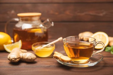 Tahta zemin üzerinde zencefil kökü dilimleri olan bir fincan sıcak zencefil çayı. Isıtıcı içecek. Alternatif tıp. Ballı, limonlu, zencefilli ve naneli çay. Mesaj için yer var. Boşluğu kopyala