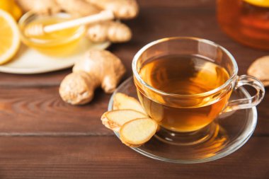 Tahta zemin üzerinde zencefil kökü dilimleri olan bir fincan sıcak zencefil çayı. Isıtıcı içecek. Alternatif tıp. Ballı, limonlu, zencefilli ve naneli çay. Mesaj için yer var. Boşluğu kopyala