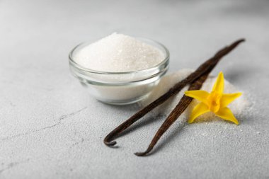 Aromatik vanilya şekeri. Vanilya kabukları. Vanilya çubukları, esmer ve beyaz şeker dokulu arka planda bir kasede. Vanilya çiçekleri, baharatlar ve tatlı ve pişirme için bitkiler. Mesaj için yer var. Boşluğu kopyala
