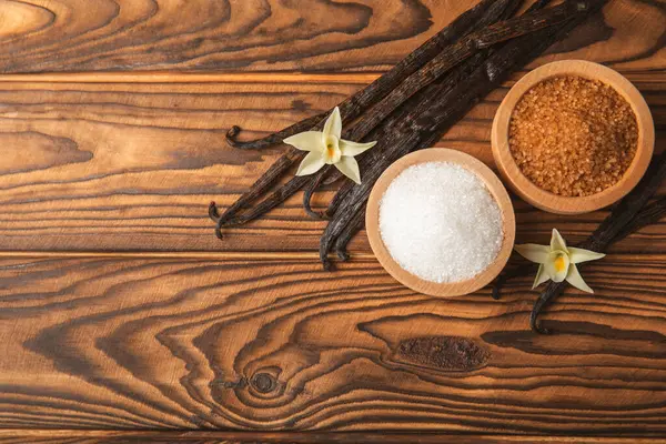 Aromatik vanilya şekeri. Vanilya kabukları. Vanilya çubukları, esmer ve beyaz şeker dokulu arka planda bir kasede. Vanilya çiçekleri, baharatlar ve tatlı ve pişirme için bitkiler. Mesaj için yer var. Boşluğu kopyala