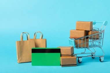 Çevrimiçi alışveriş kavramı. Karton kutu ve parlak renkli bir arka planda tramvayda alışveriş poşetleri. Alışveriş sepeti. İnternetten bilgisayar, tablet, telefon ve kredi kartı kullanarak alışveriş. Eve teslim.