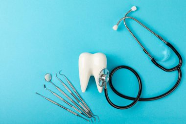 Mavi arkaplandaki dişçi aletleri. Diş hekimi konsepti. Diş bakımı, diş sağlığı konsepti. Ağız boşluğuna dikkat etmek anlamına geliyor. Diş modeli ve dişçi aletleri. Diş hijyeni. Mesaj için yer var. Boşluğu kopyala.
