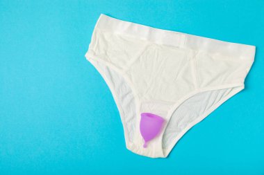 Aybaşı kupası, parlak bir arka plan. Hijyenik peçeteler, tamponlar ve regl kupası. Kritik günler, regl dönemi kavramı. Kadın hijyen ürünü. Kadın sağlığı kavramı. Adet öncesi sendromu. Boşluğu kopyala