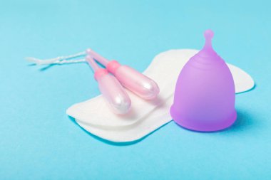 Aybaşı bardağı parlak bir arka planda. Hijyenik peçeteler, tamponlar ve regl kupası. Kritik günler, regl dönemi kavramı. Kadın hijyen ürünü. Kadın sağlığı kavramı. Adet öncesi sendromu. Boşluğu kopyala