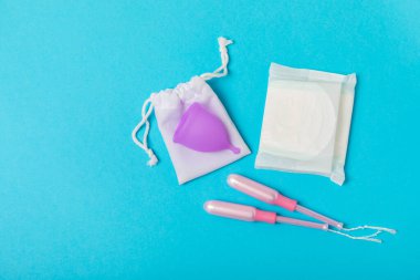 Aybaşı bardağı parlak bir arka planda. Hijyenik peçeteler, tamponlar ve regl kupası. Kritik günler, regl dönemi kavramı. Kadın hijyen ürünü. Kadın sağlığı kavramı. Adet öncesi sendromu. Boşluğu kopyala