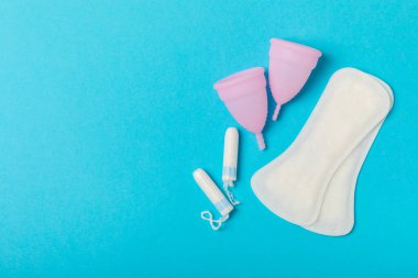 Aybaşı bardağı parlak bir arka planda. Hijyenik peçeteler, tamponlar ve regl kupası. Kritik günler, regl dönemi kavramı. Kadın hijyen ürünü. Kadın sağlığı kavramı. Adet öncesi sendromu. Boşluğu kopyala