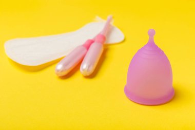 Aybaşı bardağı parlak bir arka planda. Hijyenik peçeteler, tamponlar ve regl kupası. Kritik günler, regl dönemi kavramı. Kadın hijyen ürünü. Kadın sağlığı kavramı. Adet öncesi sendromu. Boşluğu kopyala