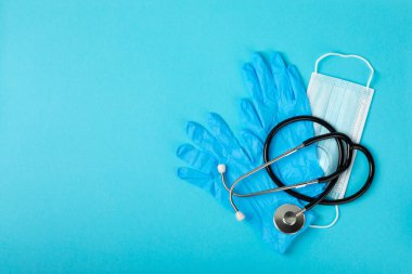 Tıbbi nitril eldivenler, mavi başlık, desenli arka planda tek kullanımlık tıbbi maske. Tıbbi koruyucu giysi. Cerrahi lateks eldivenler. Lastik eldiven üretimi. Tıp konsepti. Üst Manzara. Metni kopyala