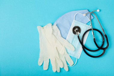 Tıbbi nitril eldivenler, mavi başlık, desenli arka planda tek kullanımlık tıbbi maske. Tıbbi koruyucu giysi. Cerrahi lateks eldivenler. Lastik eldiven üretimi. Tıp konsepti. Üst Manzara. Metni kopyala
