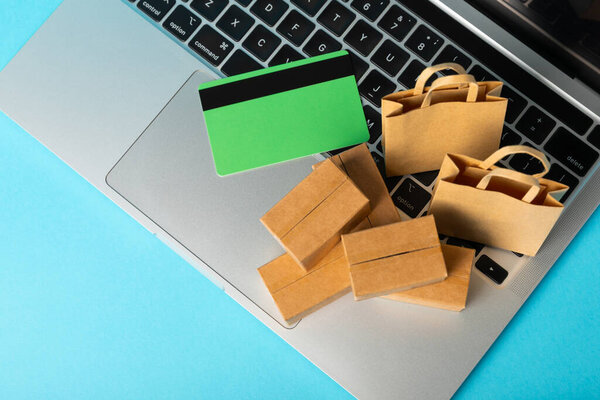 Картонная коробка и сумки для покупок в тележке на ярком фоне. Корзина покупок. Интернет-покупки с использованием ноутбука, планшета, телефона и кредитной карты. Доставка на дом.