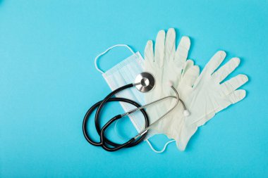 Tıbbi nitril eldivenler, mavi başlık, desenli arka planda tek kullanımlık tıbbi maske. Tıbbi koruyucu giysi. Cerrahi lateks eldivenler. Lastik eldiven üretimi. Tıp konsepti. Üst Manzara. Metni kopyala