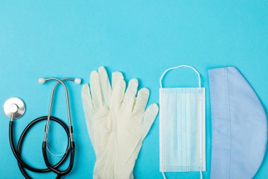 Tıbbi nitril eldivenler, mavi başlık, desenli arka planda tek kullanımlık tıbbi maske. Tıbbi koruyucu giysi. Cerrahi lateks eldivenler. Lastik eldiven üretimi. Tıp konsepti. Üst Manzara. Metni kopyala