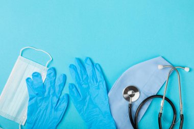Tıbbi nitril eldivenler, mavi başlık, desenli arka planda tek kullanımlık tıbbi maske. Tıbbi koruyucu giysi. Cerrahi lateks eldivenler. Lastik eldiven üretimi. Tıp konsepti. Üst Manzara. Metni kopyala
