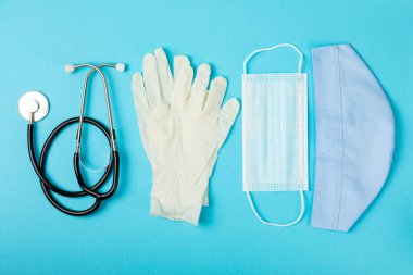 Tıbbi nitril eldivenler, mavi başlık, desenli arka planda tek kullanımlık tıbbi maske. Tıbbi koruyucu giysi. Cerrahi lateks eldivenler. Lastik eldiven üretimi. Tıp konsepti. Üst Manzara. Metni kopyala