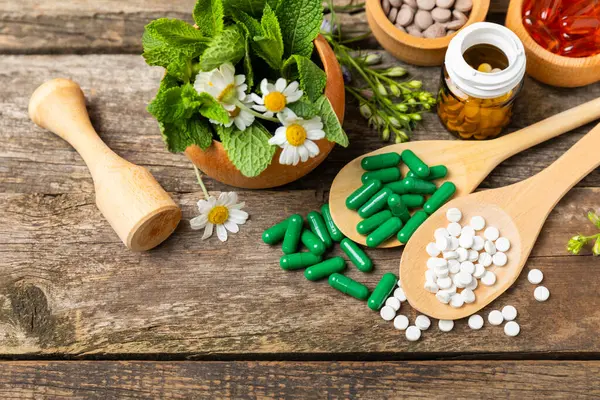 Ahşap zemin üzerinde alternatif ilaç bitkisel kapsül organik ilaç. Bitki ve tablet çeşitleri, vitaminler ve diyet takviyeleri. Sağlıklı yaşam için tıbbi ve şifalı bitkiler.
