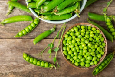 Ahşap zemin üzerinde yeşil bezelyeler olan taze bezelye kabukları. Tatlı yeşil bezelyeler. Yeşil bezelye fasulyesi sebzesi. Vejetaryen. Sağlıklı sebze. Boşluğu kopyala