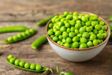 Ahşap zemin üzerinde yeşil bezelyeler olan taze bezelye kabukları. Tatlı yeşil bezelyeler. Yeşil bezelye fasulyesi sebzesi. Vejetaryen. Sağlıklı sebze. Boşluğu kopyala