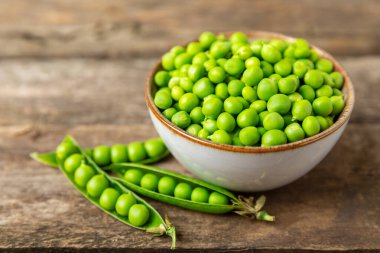 Ahşap zemin üzerinde yeşil bezelyeler olan taze bezelye kabukları. Tatlı yeşil bezelyeler. Yeşil bezelye fasulyesi sebzesi. Vejetaryen. Sağlıklı sebze. Boşluğu kopyala