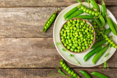 Ahşap zemin üzerinde yeşil bezelyeler olan taze bezelye kabukları. Tatlı yeşil bezelyeler. Yeşil bezelye fasulyesi sebzesi. Vejetaryen. Sağlıklı sebze. Boşluğu kopyala