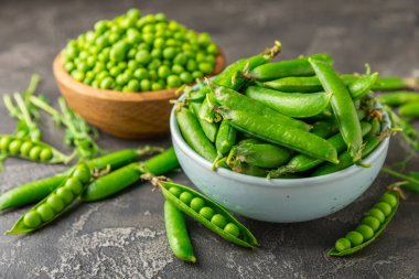 Ahşap zemin üzerinde yeşil bezelyeler olan taze bezelye kabukları. Tatlı yeşil bezelyeler. Yeşil bezelye fasulyesi sebzesi. Vejetaryen. Sağlıklı sebze. Boşluğu kopyala